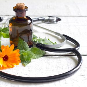 Une bouteille d'huile essentielle, une fleur de calendula et un stéthoscope, illustrant la formation en ligne de guide familial en herboristerie