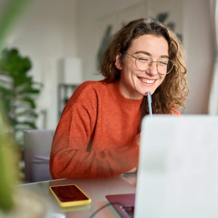 Une femme souriante devant son ordinateur, découvrant nos cours et mini-formations pour le plaisir en herboristerie.