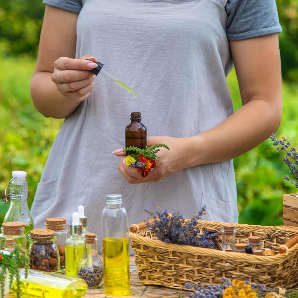Une bouteille d'huile essentielle, une fleur de lavande et diverses fleurs et huiles, illustrant la formation en ligne de guide familial en herboristerie